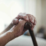 Close-up of elderly hands resting on a cane