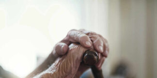 Close-up of elderly hands resting on a cane