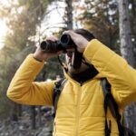 Binocular Activities Aid Aging Brains Person in a yellow jacket using binoculars in a forest
