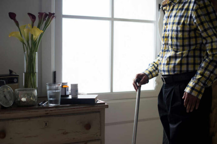 shutterstock1017555628jpg Elderly man standing with a cane next to a table with flowers and medication