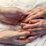 Hand-Holding: The Surprising Conflict Cooler A younger persons hand gently holding an elderly persons hand on a quilted surface