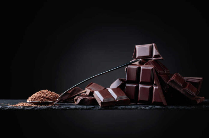 shutterstock_1105033433.jpg A pile of dark chocolate bars with cocoa powder on a black surface