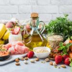 Cooking Mistakes That Steal Vital Vitamins A variety of fresh foods including fruits, vegetables, and oils arranged on a table