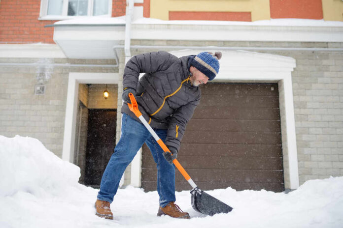Senior man shoveling snow in front of a house
