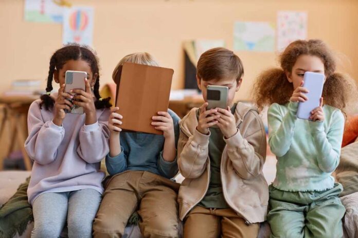 shutterstock_2307437015.jpg Four children sitting together, each focused on their electronic devices
