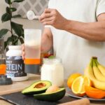 Protein Overload: How Much Is Too Much? Person preparing a protein shake with fruits and whey protein powder in a kitchen
