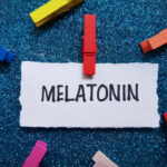 Melatonin Gummies: Hidden ER Risk for Kids A piece of paper with the word MELATONIN clipped by a red clothespin, surrounded by colorful clothespins on a blue glitter background