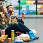 Hidden Dangers Lurking in Snack Bars A young couple sitting on the floor of a grocery store enjoying snacks