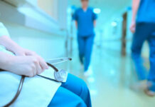 A healthcare professional holding a stethoscope in a hospital corridor