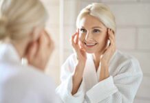 Hair Breakage or Hair Loss? Smiling woman in a bathrobe applying skincare in front of a mirror
