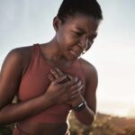 Excessive Exercise Could Steal Years from Your Life A woman in athletic wear holding her chest with a pained expression outdoors