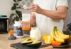 Person preparing a protein shake with fruits and whey protein powder in a kitchen