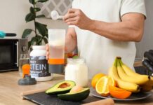 Person preparing a protein shake with fruits and whey protein powder in a kitchen