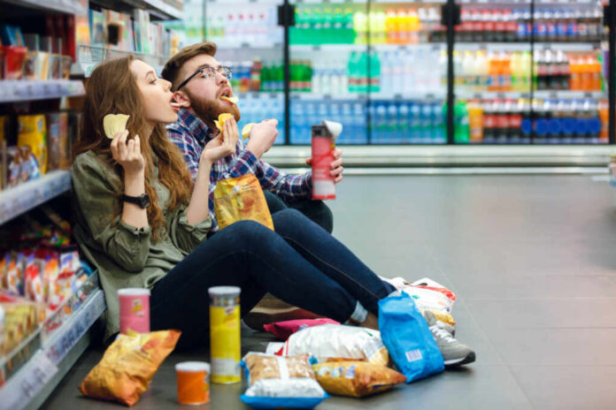 shutterstock_618433058.jpg A young couple sitting on the floor of a grocery store enjoying snacks