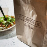 A Chipotle takeout bag next to a bowl filled with fresh salad ingredients