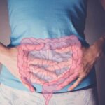 Healthy Foods That Lead To Bloating Person holding their stomach with a graphic of intestines overlayed