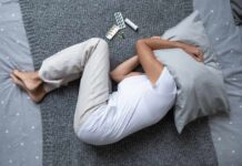 The Future of Wellness Person lying on a bed with a pillow over their head, surrounded by medication