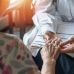 A doctor holding the hand of an elderly patient during a consultation