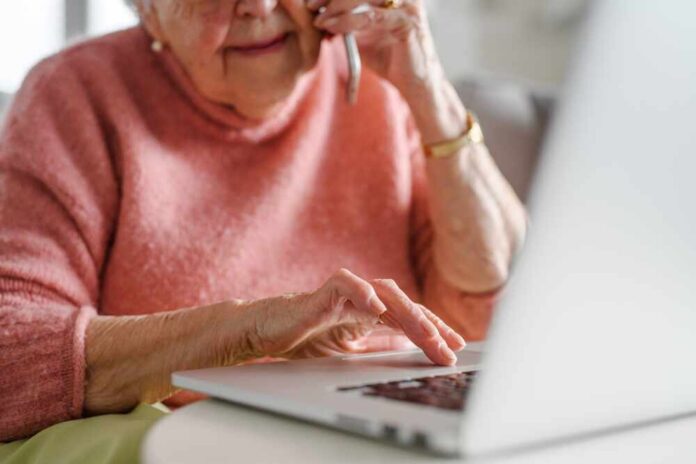 Online,And,Phone,Scams,Targeting,Seniors.,Scammer,Sending,Email,To Elderly woman on a phone call while using a laptop