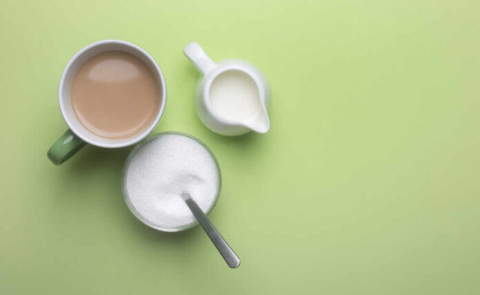 Coffee,In,A,Cup,With,Milk,With,A,Milk,Jug A cup of coffee, a bowl of sugar, and a creamer on a green background