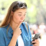 Phone Check Every 5 Minutes—Addiction or Choice? Woman looking surprised at smartphone outdoors