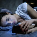 Doomscrolling Epidemic: How To Break Free Woman lying in bed looking at a smartphone