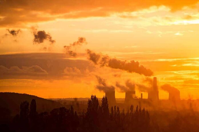 shutterstock_1645072912 Power plant cooling towers emit smoke at sunset