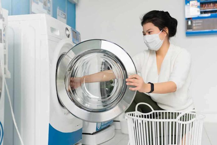 shutterstock_1765393532 Person wearing a mask loading a front‑load washing machine