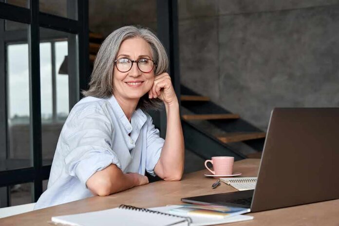 shutterstock_1824965837 Smiling woman with glasses at a desk with a laptop
