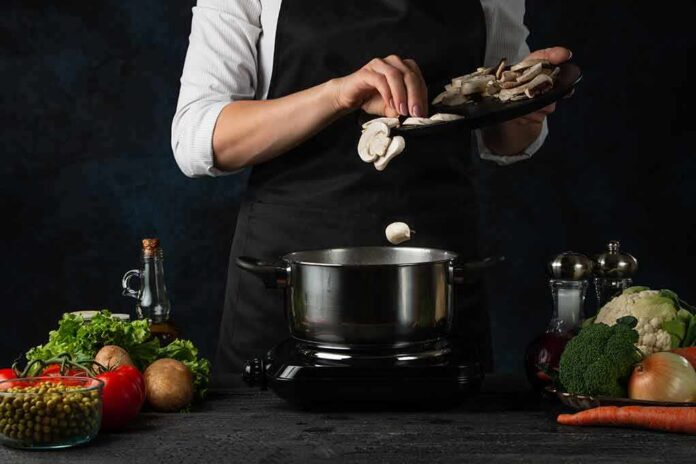 Cook adding sliced mushrooms to a pot