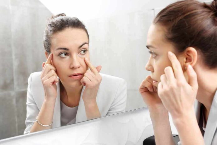 shutterstock_553579300 Woman examining her face in a bathroom mirror