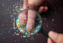 A hand holding a magnifying glass over fingers covered in colorful particles