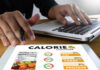 Person using a calorie counter app on a tablet while working on a laptop