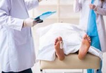 Medical staff stand near a covered body on a gurney with a toe tag