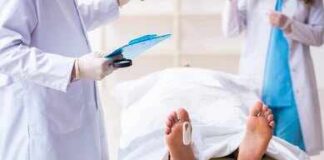 Medical staff stand near a covered body on a gurney with a toe tag