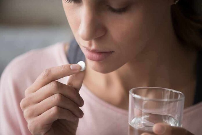 Woman holding a white pill and a glass of water