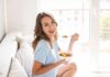 Eat This, Evade Late-Life Blues Woman sitting on a couch eating a bowl of fruit salad