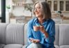 Havard-Backed Habits for Increasing Your Healthspan Smiling older woman with gray hair holding a pink coffee cup on a sofa