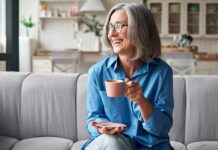 Havard-Backed Habits for Increasing Your Healthspan Smiling older woman with gray hair holding a pink coffee cup on a sofa