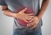 Low Liver Enzymes, Colon Cancer Spike? Person clutching stomach with colon illustration overlay