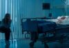 hospital room with child in bed and adult sitting nearby