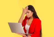 Woman in red blazer holding laptop and touching forehead