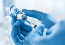 Gloved hands drawing vaccine from vial with syringe
