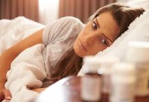 Insomnia Fix Rewinds Your DNA Clock Woman lying in bed looking at pill bottles on a bedside table