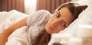 Woman lying in bed looking at pill bottles on a bedside table