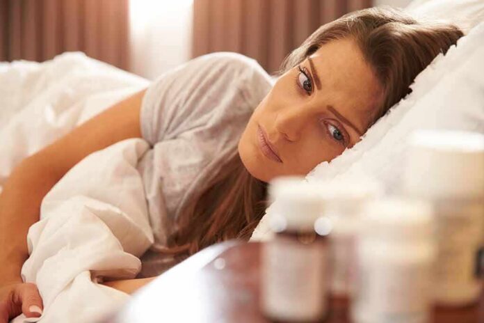 shutterstock_310310429 Woman lying in bed looking at pill bottles on a bedside table
