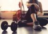 person resting on gym floor with dumbbell and water bottle