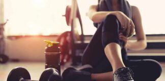 person resting on gym floor with dumbbell and water bottle