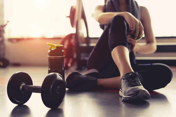 shutterstock_749969473 person resting on gym floor with dumbbell and water bottle