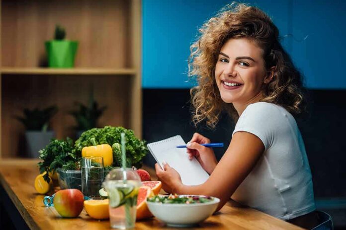shutterstock_1487265497 Smiling woman writing in a notebook at a kitchen counter with fresh produce